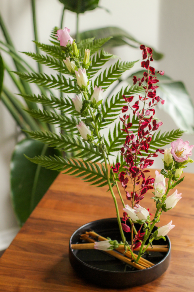 Delicate flower arrangement featuring vibrant greens and blossoms styled in Ikebana tradition on a table.