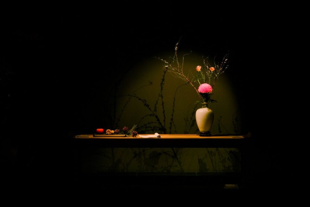 A vase with pink and orange flowers under spotlight on a wooden table with a dark background.