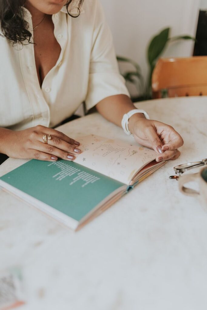 A woman reading a book at a marble table with a ring on her hand, promoting creativity and inspiration.